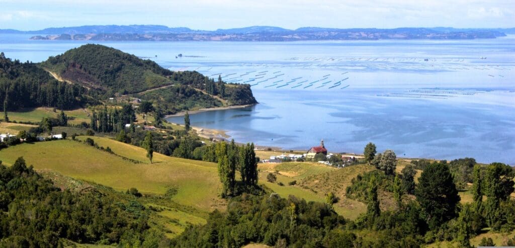 edge of a hilly lush island surrounded by calm waters and mountains in the distance