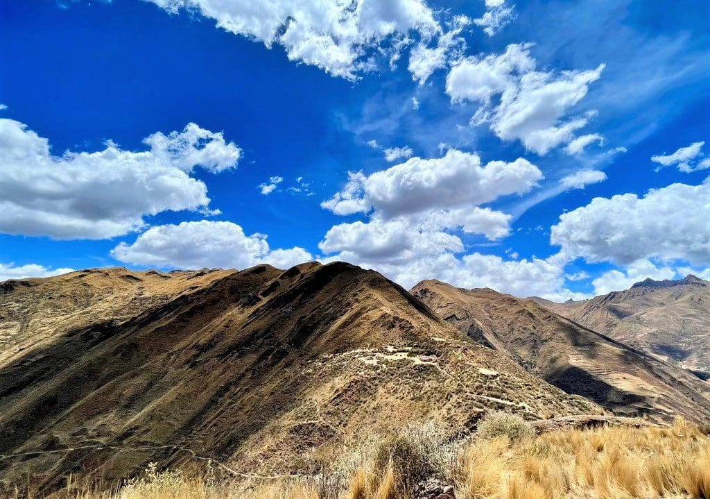 large mountains covered in dried grass and zig-zag dirt trails on a sunny, cloudy day in Peru