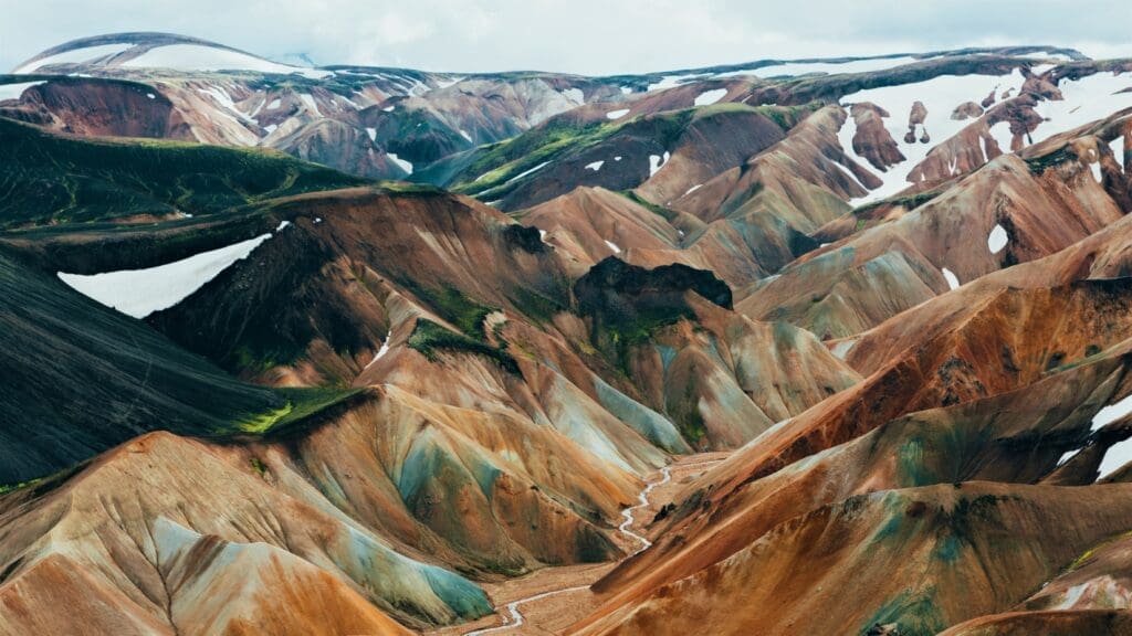 A range of snow-dusted, multi-colored rhyolite mountains with a river running through