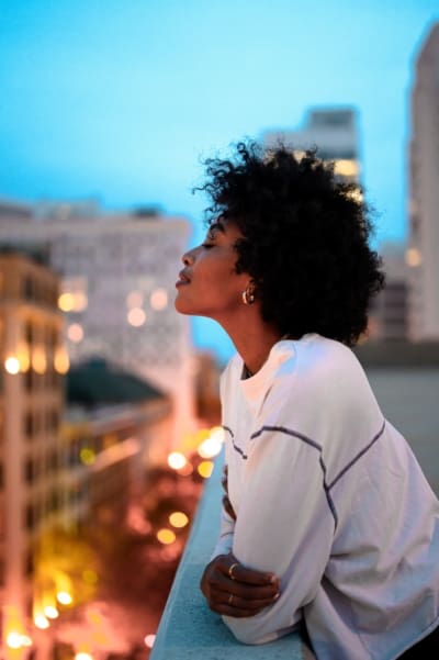 Woman smiling with her eyes closed with her head tilted toward the city night sky on a balcony.