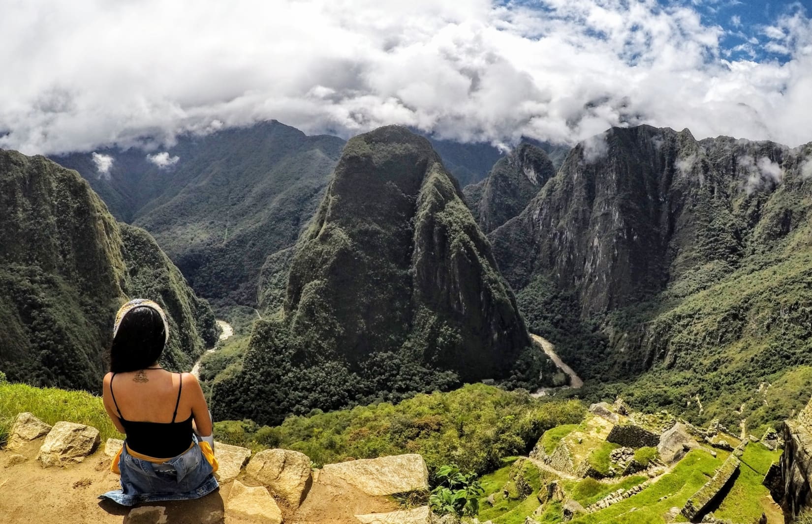 Woman sitting on a rock cliff overlooking green mountains on a cloudy day.