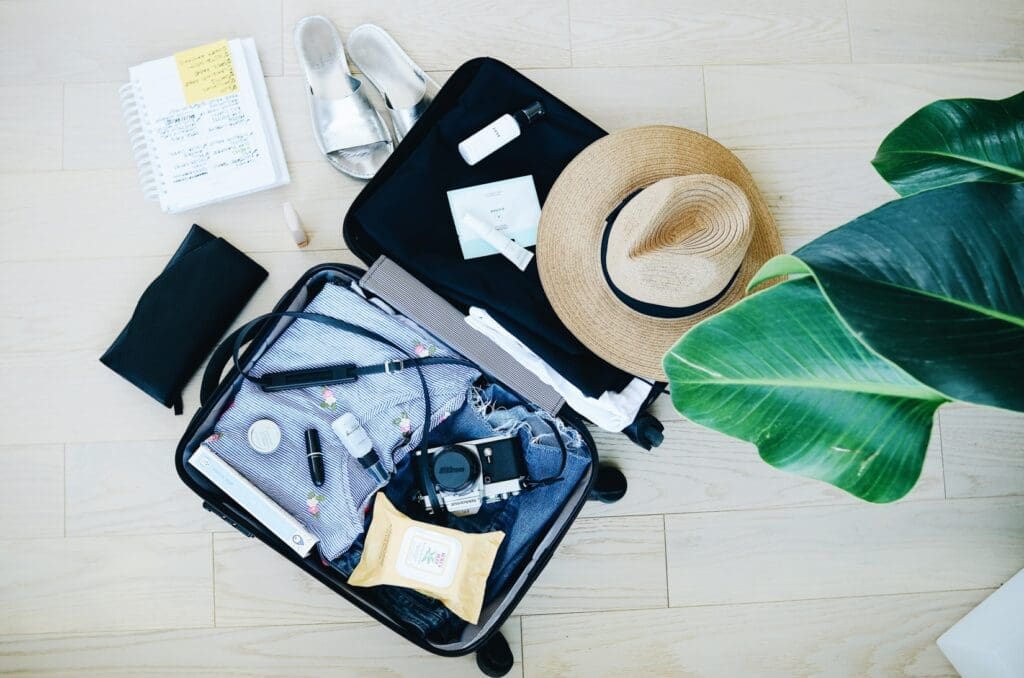 Open packed luggage with a camera and straw hat.