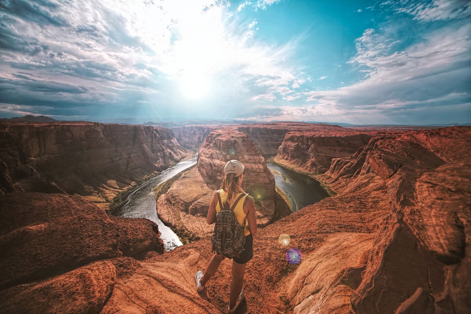 Female solo traveler with a backpack overlooking a canyon on a sunny day.