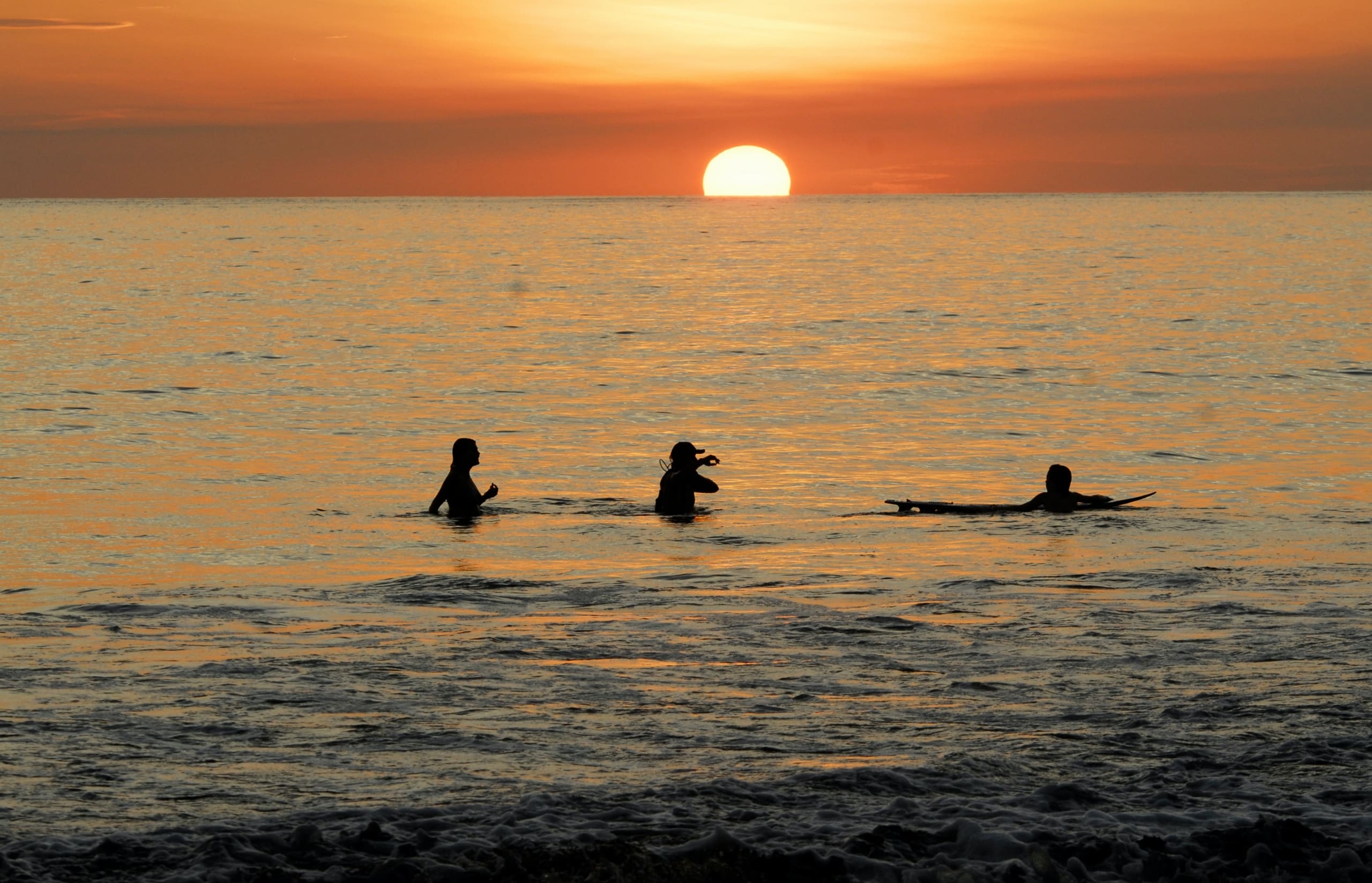 Three surfers in beach waters at sunset in Costa Rica